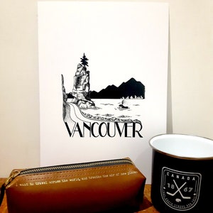 May include: A black and white illustration of a rocky island with a tree on top, a boat in the water, and the word "Vancouver" printed below. The illustration is on a white piece of paper, which is sitting on a wooden table. There is a brown leather pencil case with the text "I want to travel across the world, and breathe the air of new places" printed on it. There is also a black and white mug with the text "CANADA 1867" printed on it.