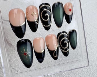 Pode incluir: Conjunto de dez unhas postiças com um design preto e verde. As unhas têm uma base preta com um design de espiral dourado e uma ponta verde. Algumas unhas têm um pequeno strass vermelho.