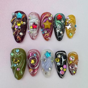 May include: Ten colourful oval-shaped nail art designs with various embellishments, including stars, swirls, and rhinestones.