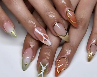 May include: Close-up of a hand with several almond-shaped nails painted with a gradient of green, orange, and white. Some nails have a gold accent and a white abstract design.