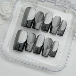 May include: A set of ten gray and white press-on nails in a clear plastic case. The nails have a glossy finish with a gradient design, transitioning from a dark gray at the base to a lighter gray and white at the tip.