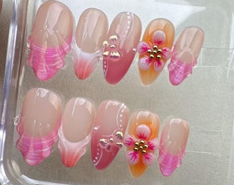 May include: A set of ten false nails with pink and white designs. The nails feature pink and white stripes, bows, and flowers with gold accents.