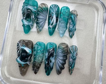 May include: A set of ten teal blue and white false nails with a fish and bubble design.