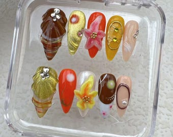 May include: A set of 10 false nails with various designs, including seashells, flowers, and abstract patterns. The nails are displayed in a clear plastic case.