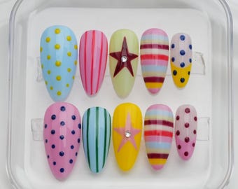 May include: A set of ten press-on nails in a clear plastic case. The nails feature various designs, including polka dots, stripes, and star accents. Colors include blue, pink, yellow, and green. Each nail is approximately 1 inch in length.