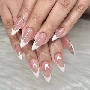 Op de afbeelding: Close-up van handen met lange, amandelvormige nagels. De nagels zijn geverfd in een lichtroze kleur met een wit, gebogen french tip-ontwerp.