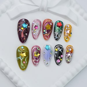 May include: A set of ten almond-shaped press-on nails featuring diverse base colors including deep purple, pink, orange, green, black, and white. Each nail is decorated with metallic silver swirls, various colorful star-shaped charms, and small rhinestones.