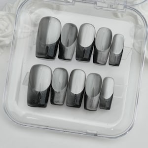 May include: A set of ten press-on nails in a clear plastic case. The nails are a gradient design, transitioning from a dark gray at the base to a lighter gray at the tip. The nails are oval-shaped.