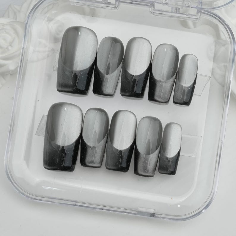 May include: A set of ten press-on nails in a clear plastic case. The nails are a gradient design, transitioning from a dark gray at the base to a lighter gray at the tip. The nails are oval-shaped.