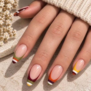 Pode incluir: Unhas em formato de amêndoa com estilo de manicure francesa, base nude e pontas multicoloridas. Cada ponta da unha exibe uma combinação única de listras horizontais em tons de verde-oliva, bordô profundo, laranja, amarelo e branco.