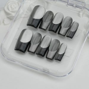 May include: A set of ten gray and black press-on nails in a clear plastic case. The nails have a glossy finish with a gradient design, transitioning from black at the base to gray at the tip. The nails are in various sizes.