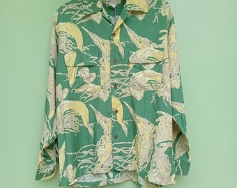 May include: A green long-sleeved shirt with a yellow and white floral pattern. The shirt has a button-up front and a collar.
