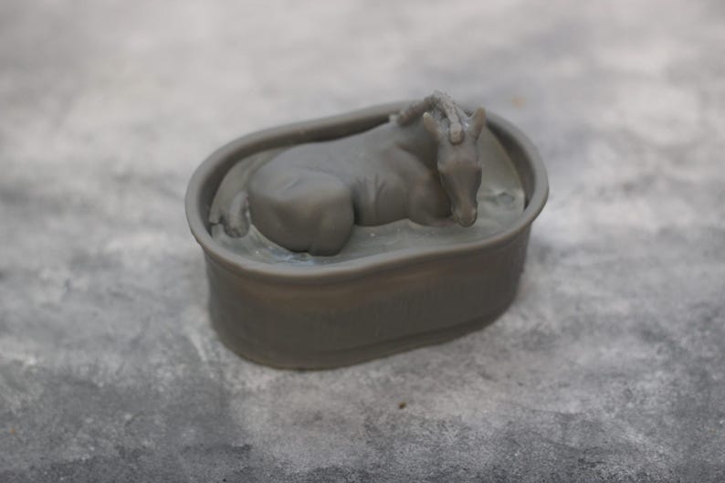 May include: A gray figurine of a horse resting in a bathtub. The horse is lying down with its head resting on its front legs. The bathtub is oval-shaped and has a simple design. The figurine is made of a solid material.