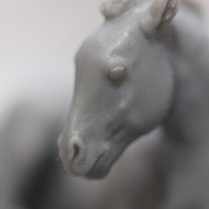 May include: A close-up of a gray horse figurine. The horse's head is in focus, showing details of the eye, nose, and ear. The figurine appears to be made of a smooth material, with subtle variations in color and texture.