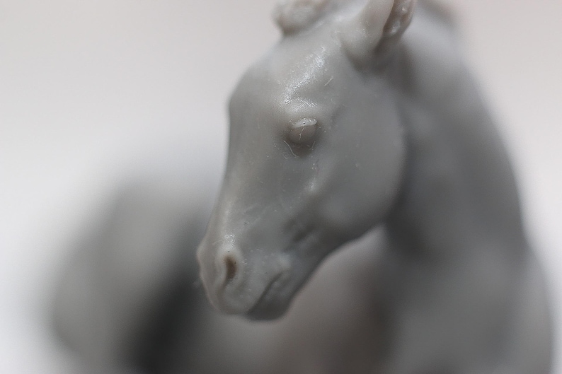 May include: A close-up of a gray horse figurine. The horse's head is in focus, showing details of the eye, nose, and ear. The figurine appears to be made of a smooth material, with subtle variations in color and texture.