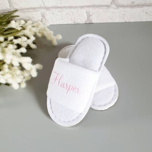 May include: White terry cloth slippers with the name "Harper" embroidered in pink on the top of one slipper.