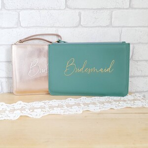 May include: Two zippered pouches, one gold and one teal, with the words "Bride" and "Bridesmaid" written in gold and white lettering.