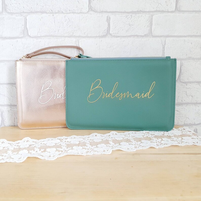 May include: Two zippered pouches, one gold and one teal, with the words "Bride" and "Bridesmaid" written in gold and white lettering.