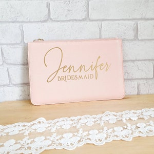 May include: A pale pink zippered pouch with the name "Jennifer" and the word "BRIDESMAID" written in gold lettering.