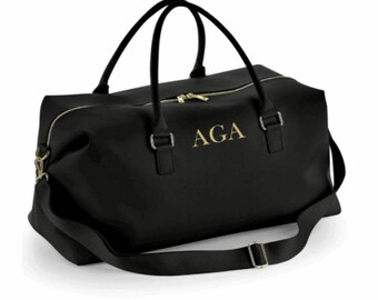 May include: Black leather travel duffel bag with a gold zipper and a gold monogram that reads "AGA".
