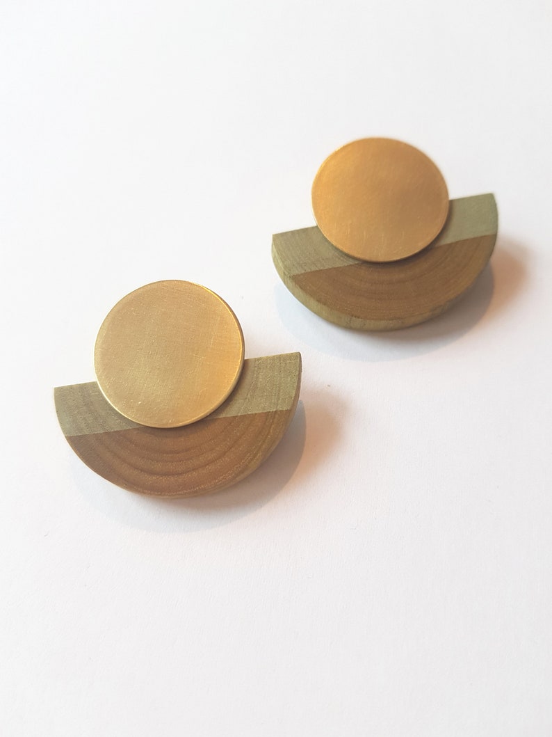 Puede incluir: Un par de pendientes de oro y madera. Cada pendiente tiene un disco redondo de oro sobre un semic&iacute;rculo de madera.