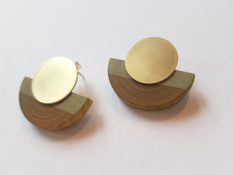 Puede incluir: Un par de pendientes geom&eacute;tricos con un c&iacute;rculo de lat&oacute;n sobre un semic&iacute;rculo de madera.