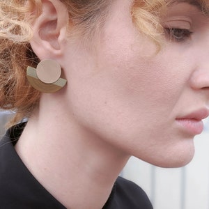 Puede incluir: Un par de pendientes geom&eacute;tricos con forma de semic&iacute;rculo y un c&iacute;rculo en el centro. Los pendientes est&aacute;n hechos de madera y tienen un esquema de color marr&oacute;n claro, beige y verde.