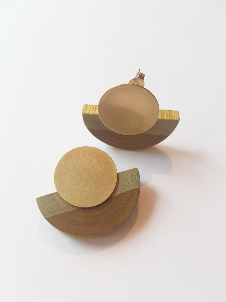 Puede incluir: Un par de pendientes de oro y madera. Cada pendiente tiene un disco redondo de oro sobre un semic&iacute;rculo de madera.