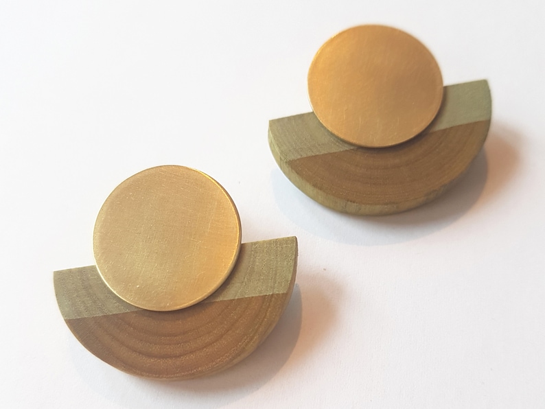 Puede incluir: Un par de pendientes de oro y madera. Cada pendiente tiene un disco redondo de oro sobre un semic&iacute;rculo de madera.