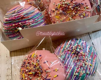 May include: A box of six pink and white frosted donuts with colorful sprinkles. The donuts are in individual clear plastic bags. The box has the text "@treatsbytasha" printed on it.