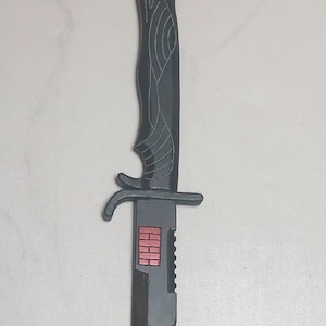 May include: A black plastic sword with a decorative handle and a red and white design on the blade.