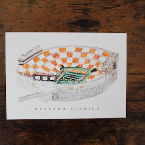 Pu&ograve; includere: Un'illustrazione ad acquerello del Neyland Stadium, casa della squadra di football americano dei Volunteers dell'Universit&agrave; del Tennessee. Lo stadio &egrave; rappresentato in una vista aerea, mostrando i sedili arancioni e bianchi e il campo verde.