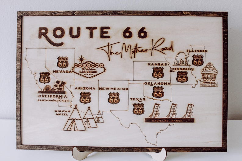 Puede incluir: Un letrero de madera con un mapa de la Ruta 66, con el texto "Route 66 The Mother Road" y varios puntos de referencia a lo largo de la ruta, incluido el Wigwam Motel, Cadillac Ranch y el muelle de Santa M&oacute;nica.