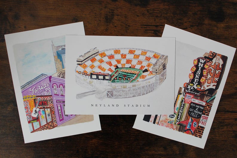Pu&ograve; includere: Tre stampe illustrate di uno stadio di calcio, un edificio con una chitarra e il testo "Tootsies", e un edificio con il testo "Whiskey Be Here" e "Authentic", con il testo "Buy One Pint & Get One Free" su un cartello.