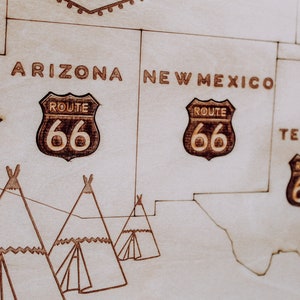 Puede incluir: Un mapa de madera de los Estados Unidos con la Ruta 66 resaltada en marr&oacute;n. El mapa muestra los estados de Arizona, Nuevo M&eacute;xico, Texas y Oklahoma. Las palabras "Ruta 66" est&aacute;n escritas en marr&oacute;n en el mapa. Tambi&eacute;n hay tres tipis dibujados en el mapa.