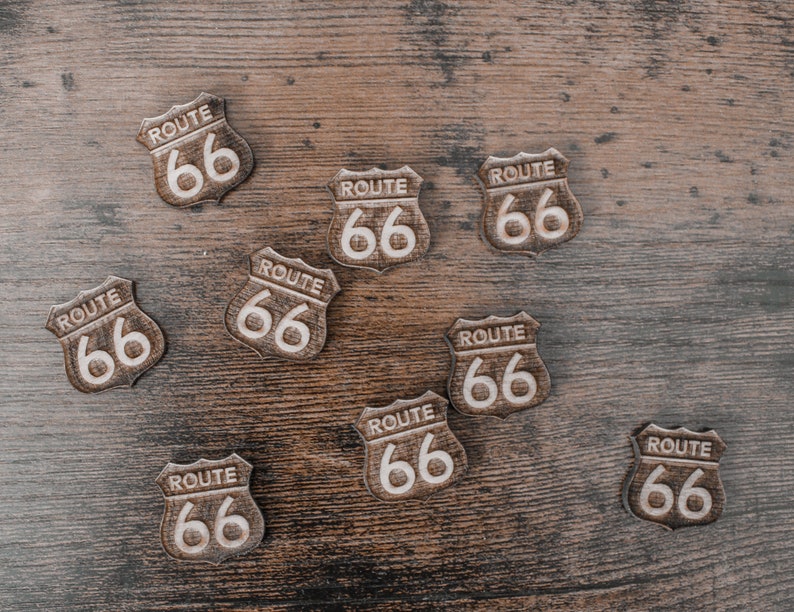 Puede incluir: Ocho se&ntilde;ales de madera de la Ruta 66 sobre un fondo de madera marr&oacute;n. Cada se&ntilde;al tiene forma de escudo y tiene el texto "ROUTE 66" en letras blancas.