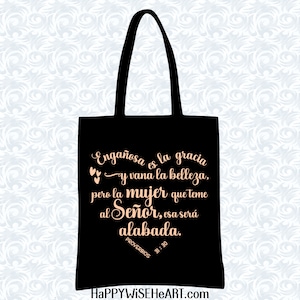 May include: Black tote bag with a scripture quote in Spanish. The quote reads "Enga&ntilde;osa es la gracia y vana la belleza, pero la mujer que teme al Se&ntilde;or, esa ser&aacute; alabada." The bag has black handles and the website HAPPYWISEHEART.com is at the bottom.