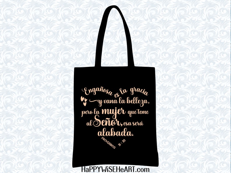 May include: Black tote bag with a scripture quote in Spanish. The quote reads "Enga&ntilde;osa es la gracia y vana la belleza, pero la mujer que teme al Se&ntilde;or, esa ser&aacute; alabada." The bag has black handles and the website HAPPYWISEHEART.com is at the bottom.