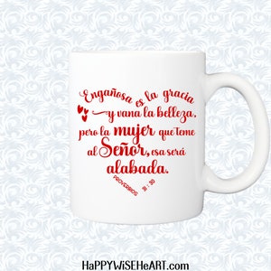 May include: White ceramic mug with a curved handle. The mug features red script that reads "Enga&ntilde;osa es la gracia y vana la belleza, pero la mujer que teme al Se&ntilde;or, esa ser&aacute; alabada. PROVERBIOS 31:30". The website HAPPYWISEHEART.com is at the bottom.