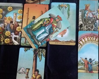 May include: Tarot card spread with ten cards, including the King of Cups, Ace of Swords, and Judgement cards. The cards are laid out in a cross pattern on a dark blue surface.