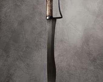 May include: A curved sword with a dark blade and a detailed handle. The handle features a gold-colored section with intricate patterns and a dark brown grip. A curved guard extends from the handle.