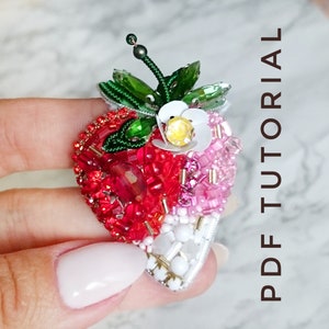 May include: A beaded strawberry brooch with red, pink, and white beads, a green beaded stem, and a white flower with a yellow center.
