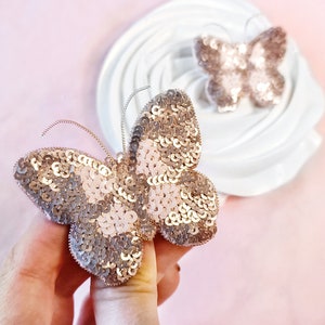 May include: A gold and pink sequined butterfly brooch. The butterfly has a delicate design and is perfect for adding a touch of sparkle to any outfit.
