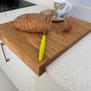 Sliced seeded bread and a coffee cup on a solid oak worktop protector, highlighting its large surface area and secure edge-of-counter design.