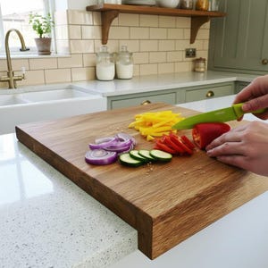 Hands slicing a red pepper on a thick solid oak worktop protector, alongside sliced red onions, yellow peppers, and cucumbers. The image highlights the natural wood grain and the secure edge-of-counter lip design.