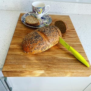Sliced seeded bread and a coffee cup on a solid oak worktop protector, highlighting its large surface area and secure edge-of-counter design.