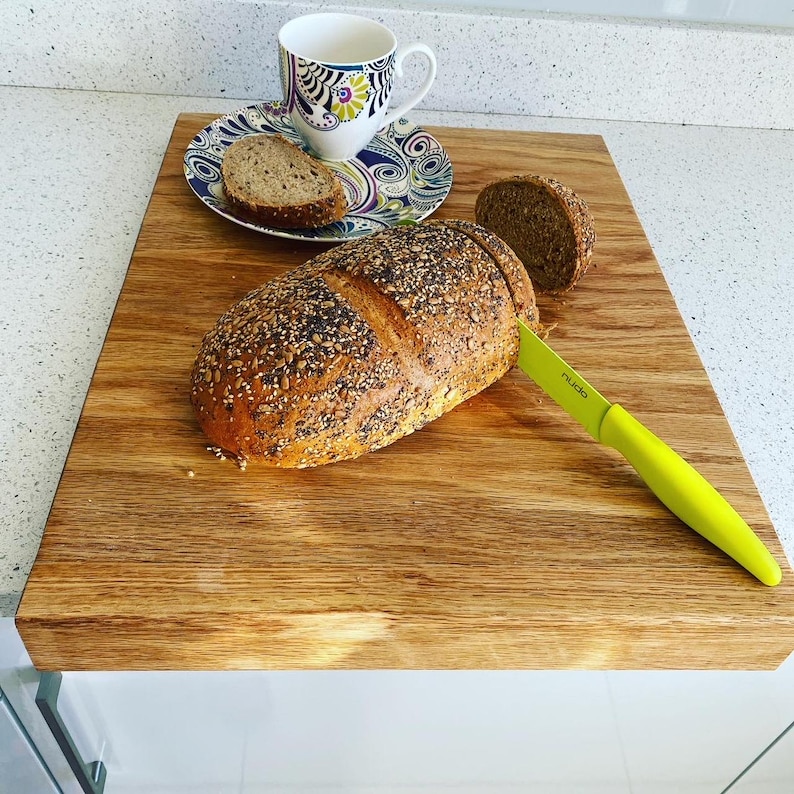 Sliced seeded bread and a coffee cup on a solid oak worktop protector, highlighting its large surface area and secure edge-of-counter design.