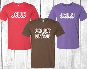 May include: Three t-shirts with a retro font design. One red t-shirt says "JELLY", one purple t-shirt says "JELLY", and one brown t-shirt says "PEANUT BUTTER".