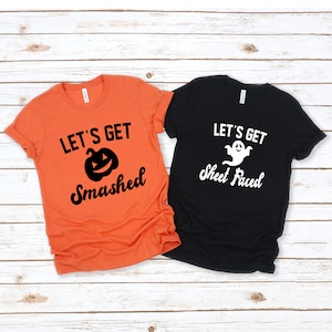 May include: Two t-shirts with Halloween-themed text and graphics. The orange shirt says "Let's Get Smashed" with a black pumpkin graphic. The black shirt says "Let's Get Sheet Faced" with a white ghost graphic.