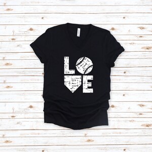 May include: Black V-neck t-shirt with a white graphic that says "LOVE" with a baseball replacing the "O". The baseball design has white stitching details. The shirt is made of a soft material.